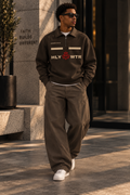 Model wearing a brown HLY WTR quarter-zip with cream lettering, red HW crown crest, and Romans VIII:VI detail.