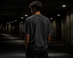 Back view of HLY WTR oversized black tee with plain design in dark urban tunnel