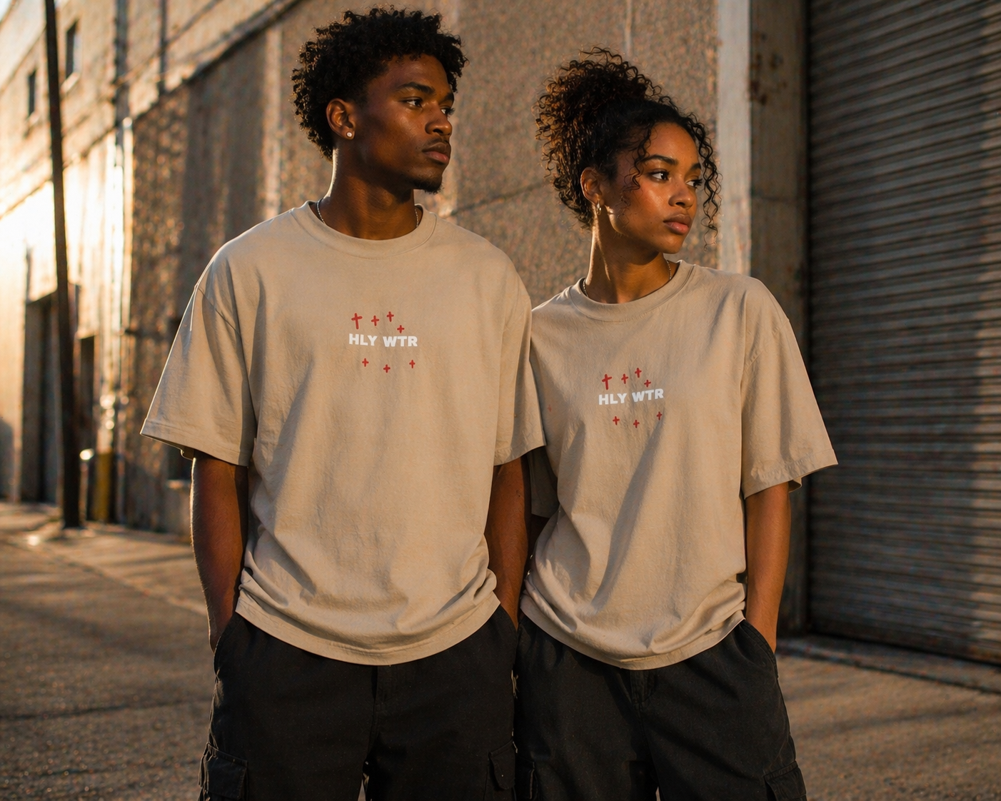 African American male and female models wearing HLY WTR oversized stone color tees in warm urban street setting
